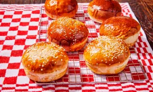 Petits pains à burger dorés et moelleux, certains parsemés de graines de sésame, sur une grille de refroidissement.