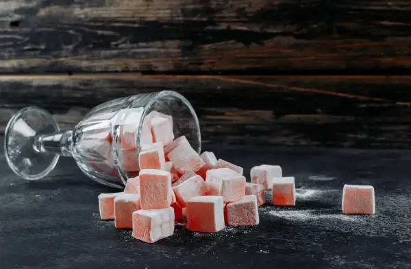 Un verre renversé d'où tombent des cubes de loukoum roses saupoudrés de sucre glace.